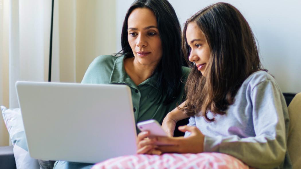 Mother and daughter looking at a laptop and cell phone together